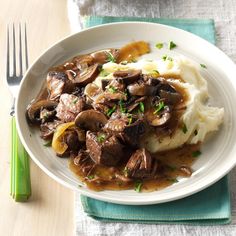 a white plate topped with mashed potatoes covered in mushrooms and gravy next to a fork