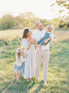 a man and woman holding two small children while standing in the grass