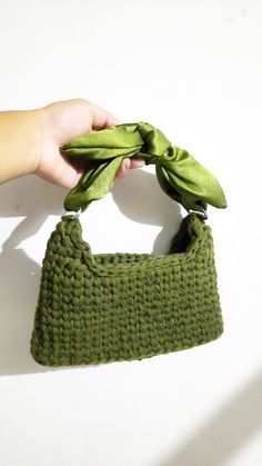 a hand holding a green purse on top of a white wall with a knot in it