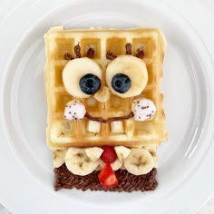 a plate with waffles and fruit on it that has a face made out of bananas