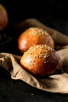 three bread rolls sitting on top of a brown cloth next to some other food items