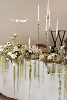 a table topped with lots of white flowers and greenery next to tall candle holders