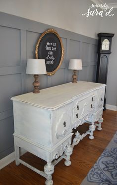 a white dresser with two lamps and a chalkboard sign on the wall behind it