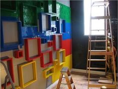 there is a ladder next to a wall with different colored blocks on it and a window in the background