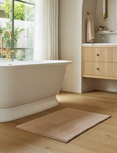 a white bath tub sitting on top of a hard wood floor next to a window