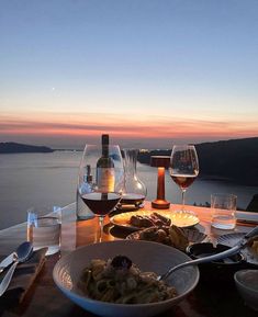 two glasses of wine are sitting on a table with food and drinks in front of the ocean