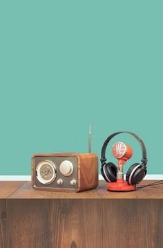 an old radio and headphones on top of a wooden table in front of a blue wall