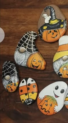 painted rocks with faces and pumpkins are arranged on a wooden surface, including one for halloween