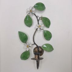 a green and white wall mounted clock with flowers on it's face, hanging from a metal hook