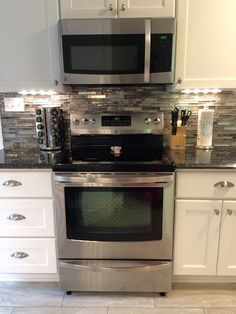 a stainless steel oven and microwave in a kitchen with white cabinets, granite counter tops and tile backsplash