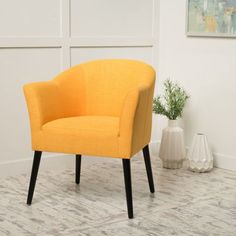 an orange chair sitting on top of a wooden floor next to a white vase filled with flowers