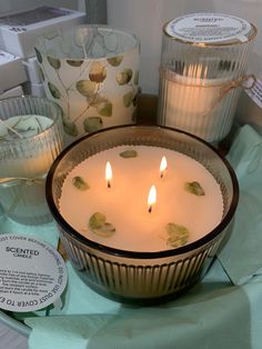 three candles sitting on top of a table next to some glass vases with leaves