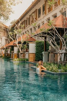 a woman sitting in the middle of a swimming pool next to buildings and trees on either side