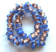 two blue and gold bracelets sitting on top of a white cloth covered tablecloth