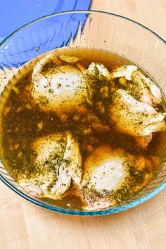 a glass bowl filled with chicken and broth sitting on top of a wooden table