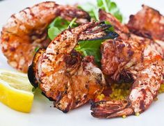 grilled shrimp on a white plate with lemon wedges and garnished greens