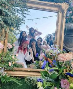 a group of women taking a selfie in front of a mirror with flowers and greenery