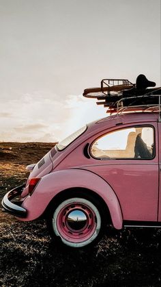 a pink vw bug with a surfboard on the roof is parked in a field