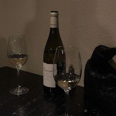 a bottle of wine and two glasses on a table with a black bag in the background