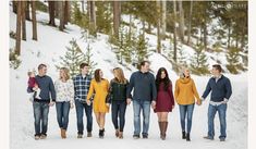 a group of people standing in the snow holding hands and looking at each other with trees behind them