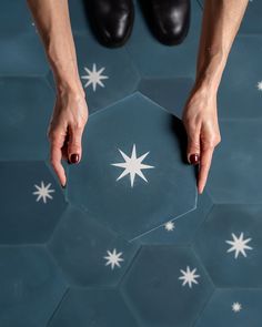 a person's hands on top of a blue tile floor with white snowflakes