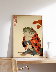 a frog with an orange and black scarf on it's back sitting in front of a white vase