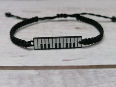 a black string bracelet with a white piano key on it, sitting on top of a wooden table