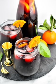 two glasses filled with liquid and garnished with orange peels on a tray