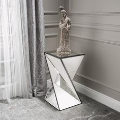 a glass table with a statue on top in front of a curtained room window