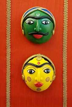 two masks are hanging on a red wall and one is painted green, the other has yellow