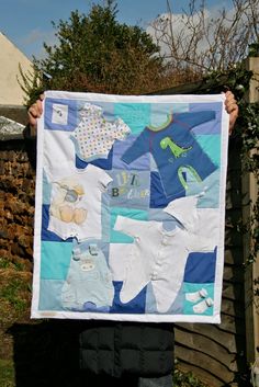 a person holding up a quilt with baby clothes on it