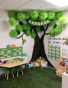 an office decorated in green and white with a tree on the wall, desks and children's toys