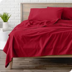 a bed with red sheets and pillows in a room next to a white brick wall