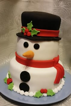 a snowman cake is decorated with holly and red ribbon on the top, while wearing a black hat