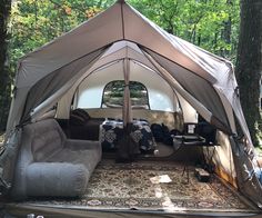 the inside of a tent with couches and pillows in it, surrounded by trees