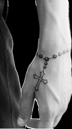 a man and woman holding hands with a cross tattoo on their wrist, while the other hand has a rosary attached to it