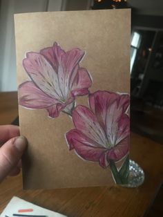 a person holding up a card with some flowers painted on the front and back of it