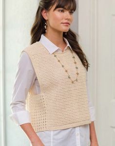 a woman standing in front of a door wearing a white shirt and beige knitted vest