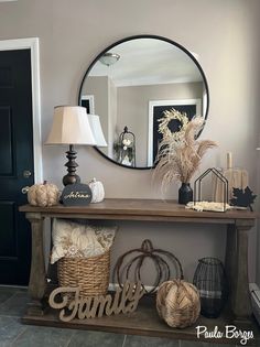 a wooden table topped with a mirror and baskets filled with pumpkins next to a lamp