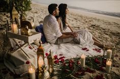 a man and woman sitting on the beach next to each other with candles in front of them