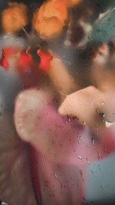 a blurry image of rain on a window with red and yellow umbrellas in the background