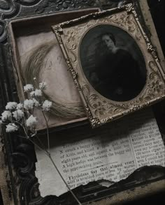 an old photo frame with flowers on top of it next to a book and paper