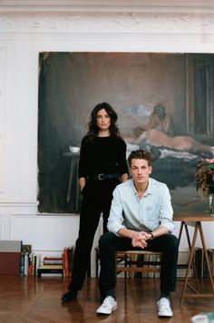 a man and woman sitting in front of a painting