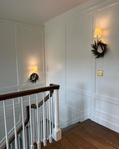 a staircase with two wreaths on the wall next to it and another light that is on