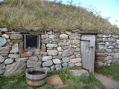 an old stone building with a grass roof and door in the middle of it's yard