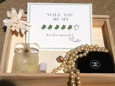 a wooden box with pearls and perfumes in it, including a card that says will you be my bridesmaid?