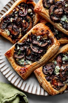 four puff pastry topped with mushrooms and blue cheese on a plate next to a green napkin