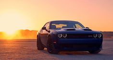 the front end of a blue sports car parked in an empty lot at sunset with mountains in the background