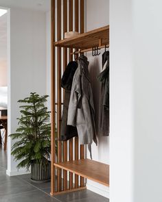 a coat rack with two coats hanging on it and a potted plant next to it