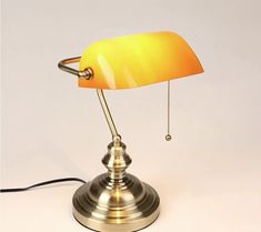 a lamp with a yellow shade sitting on top of a white table next to a black cord